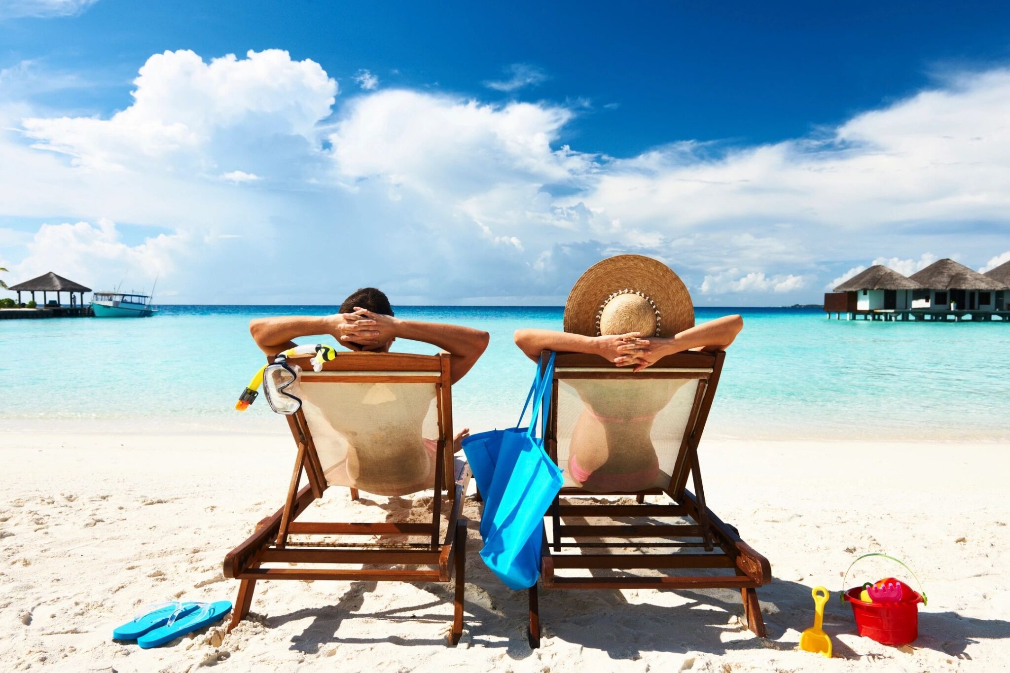 Travelers relaxing in beach chairs beside turquoise water at a tropical resort